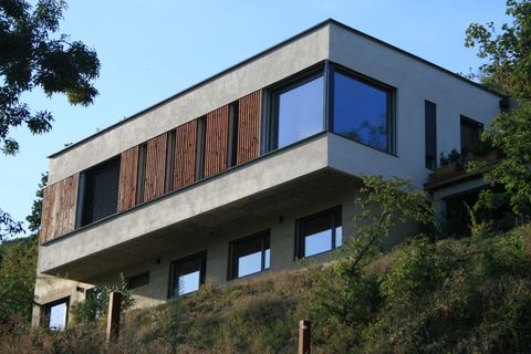 Maison contemporaine à deux niveaux, l'étage en porte-à-faux au-dessus de la pente, bardage bois et enduit clair