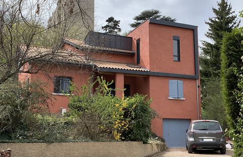 Maison au crépi rouge surélevée d'un volume à toit plat, vue depuis la rue